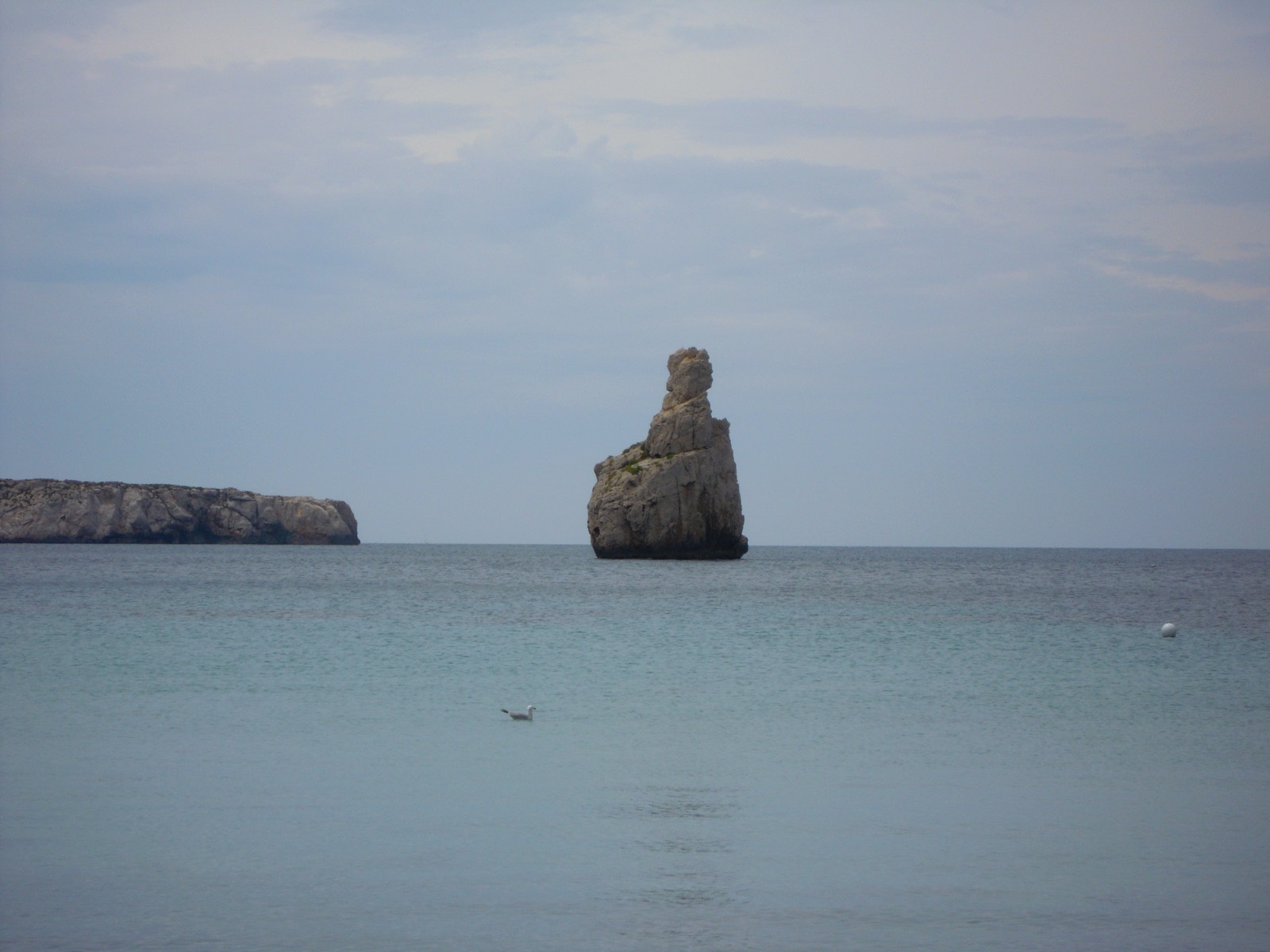 The small cove of Benirras in northern Ibiza, with a rocky islet offshore and pine covered slopes around the bay