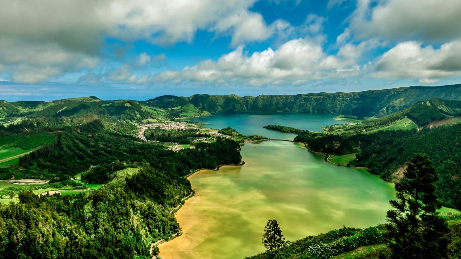 The green crater lake of Sete Cidades on Sao Miguel in the Azores, ringed by steep forested slopes under a soft sky.