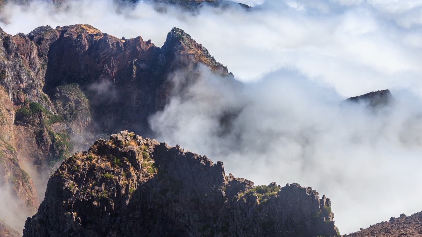 The bare rock peaks around Pico do Arieiro in Madeira rising above a thick floor of cloud, lit by early sun.